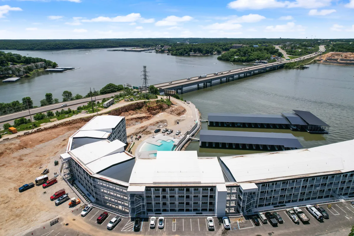 A striking view of the hotel's curved architecture overlooking a swimming pool, with the nearby waterway and a bridge visible in the background. The scene exudes a sense of tranquility and recreational opportunity, with open skies and scenic surroundings.