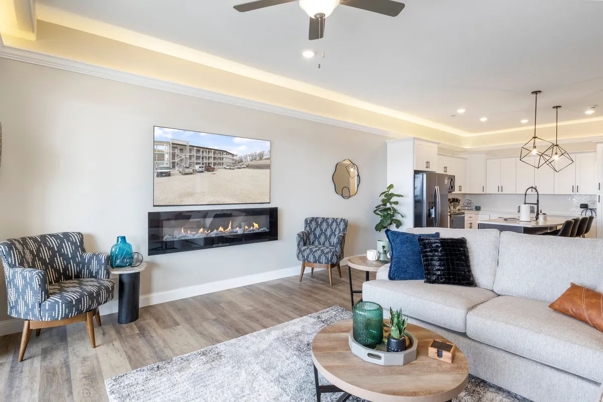 An inviting living room centers around a glowing fireplace, with a plush sofa, television, decorative chairs, and a coffee table creating a cozy gathering space. The mood is warm and welcoming, ideal for indoor relaxation.