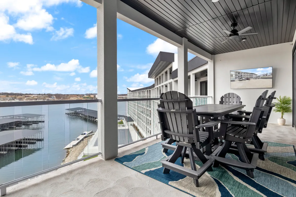 A spacious outdoor dining table and Adirondack chairs are set up on a private balcony, with a sweeping water view beyond. The setting is perfect for sunset dinners, morning coffee, or quiet moments taking in the scenery. The decorative rug and stylish outdoor furniture add a touch of comfort and elegance.
