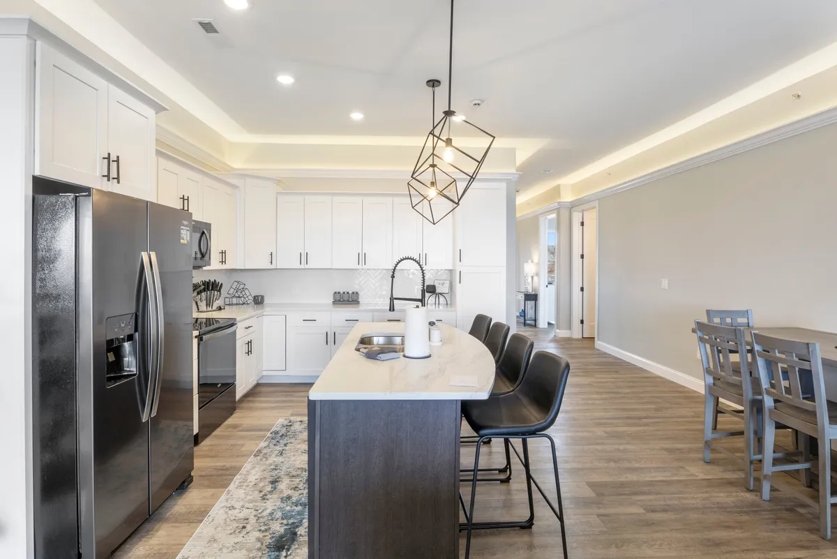 A contemporary open-concept kitchen with a spacious island, modern appliances, and a large dining table set for group meals. The area is well-lit and inviting, ideal for cooking, entertaining, and celebrating together.