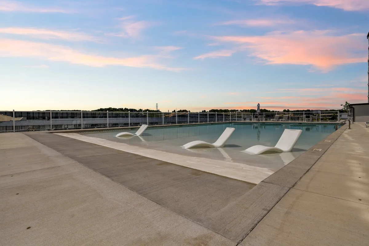 An infinity pool invites guests to swim or lounge while gazing at the lake. Arranged lounge chairs face the water, and the sky glows with hues of sunset. The pool area is lively yet peaceful, suggesting both social gatherings and solitary relaxation.
