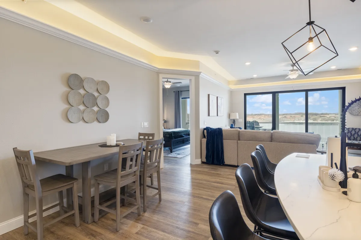 A broad view of the open-plan living and dining area, highlighting a modern dining table, comfortable sofa, and floor-to-ceiling windows that frame spectacular lake scenery. The layout encourages seamless flow between relaxation and shared meals.