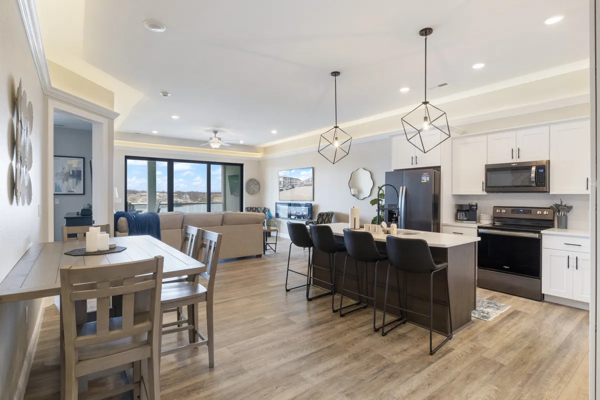 This image captures a contemporary and cozy space featuring a kitchen island, dining table, large windows, and visible living area seating. The setup invites socializing, board games, and shared dining against the backdrop of natural beauty.