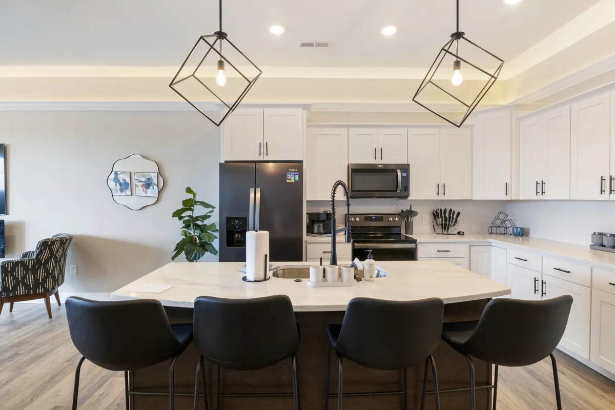 This photo presents a contemporary kitchen with a central island countertop, bar stools for casual seating, and sleek kitchen appliances. Warm lighting and thoughtful decor make it an inviting spot for cooking together, enjoying a morning coffee, or gathering for snacks. The kitchen's open design hints at a seamless connection to the adjoining dining area or living spaces.