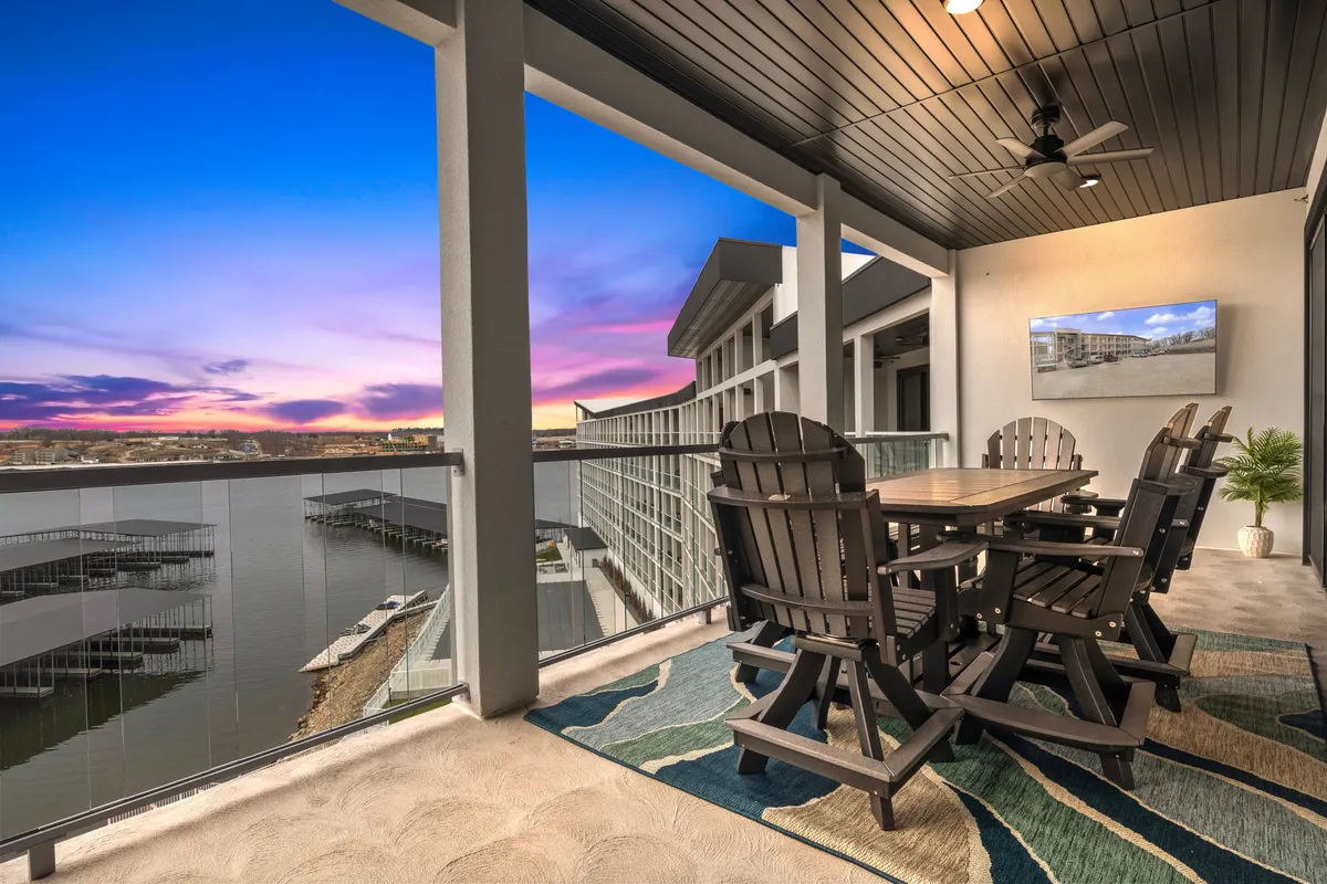 The balcony is arranged with a dining table and Adirondack chairs, all oriented to maximize enjoyment of the water view and sunset sky. The scene radiates tranquility and is perfect for outdoor dining, entertaining, or unwinding with a morning coffee or evening cocktail while watching boats pass by.