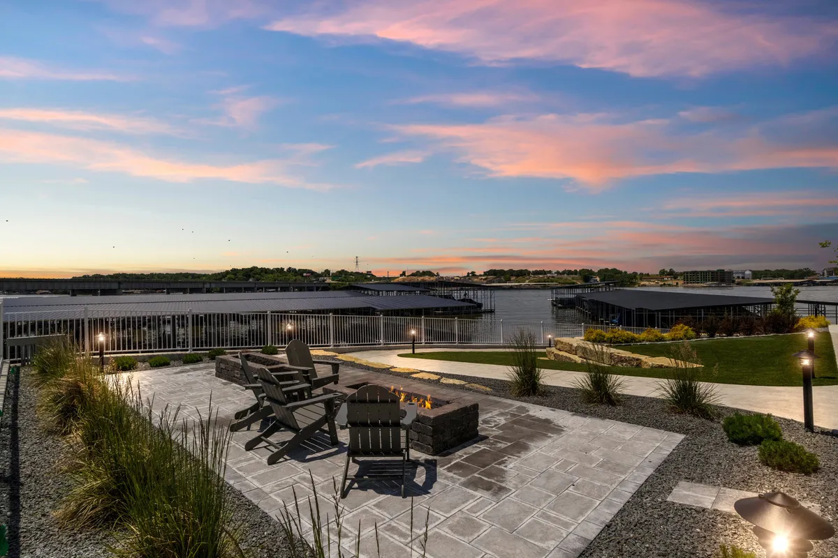 A cozy waterfront fire pit area surrounded by Adirondack chairs, overlooking a tranquil lake view. The setting is perfect for evening gatherings, storytelling, and creating memories by the water.